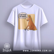 Футболка кінь don't push, біла футболка на вішалці, ракурс спереду, фон світло-сірий, принт з зображенням коня, що сидить, з текстом 'DON'T PUSH THE HORSES' у бульбашці.