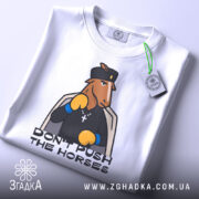 Футболка кінь don't push, біла, зображена зверху, фон світло-сірий, принт з конем у чорному костюмі та капелюсі, з боксерськими рукавичками, на футболці є етикетка з логотипом.