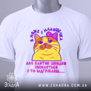 Футболка кішка малишечка, біла, зображена зверху, фон світло-сірий, принт з жовтою кішкою з рожевим бантиком та текстом, на футболці є етикетка з зеленим шнурком.