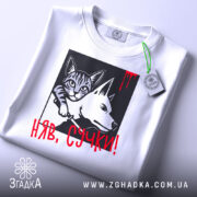 Футболка кіт бунтар, біла, складена на поверхні, фон світло-сірий, принт з котом і собакою в чорному квадраті, червоний напис 'НЯВ, СУЧКИ!' з краплинами червоного, на комірці є етикетка.