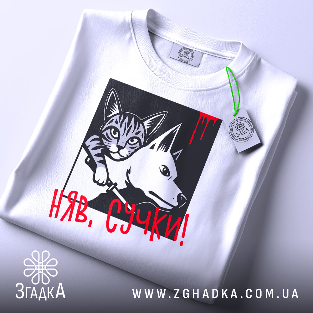 Футболка кіт бунтар, біла, складена на поверхні, фон світло-сірий, принт з котом і собакою в чорному квадраті, червоний напис 'НЯВ, СУЧКИ!' з краплинами червоного, на комірці є етикетка.