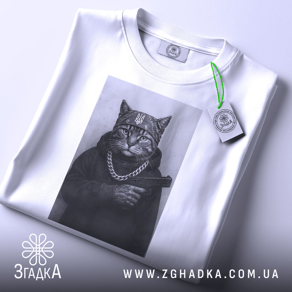 Футболка кіт гангстер стиль, біла футболка з принтом кота в гангстерському стилі, ракурс зверху, фон світло-сірий, принт зображує кота в капелюсі та з пістолетом, на шиї ланцюг, з етикеткою.