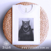 Футболка кіт гангстер стиль, біла футболка з принтом кота в гангстерському стилі, ракурс зверху, фон світло-сірий, принт зображує кота в капелюсі та з пістолетом, на шиї ланцюг, лежить на плетеній основі.