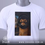 Футболка кіт геймер, біла, зображена зверху, на фоні світло-сірого градієнту, принт з котом у навушниках та масці геймера, з виразними очима, прикріплена етикетка з зеленим шнурком.