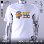 Футболка кіт готує, біла, з фронтального ракурсу, на манекені, з яскравим принтом кота в кухарському ковпаку, що тримає лопатку, текстом 'KIT готує краще всіх!' у жовтому та блакитному кольорах.