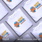 Футболка кіт готує, біла, з фронтального ракурсу, на манекені, з яскравим принтом кота в кухарському ковпаку, що тримає лопатку, текстом 'KIT готує краще всіх!' у жовтому та блакитному кольорах.