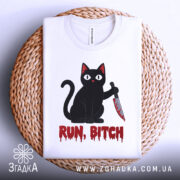 Футболка кіт маніяк, біла, складена на плетеній кошику, фон світлий, принт чорного кота з ножем і написом 'RUN, BITCH' червоним кольором.