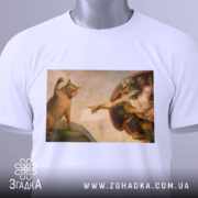 Футболка кіт Мікеланджело, біла, зображена на столі, фон світло-сірий, принт з котом і людиною в стилі Мікеланджело, на футболці є етикетка з зеленим шнурком, деталі малюнка чітко видимі.