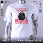 Футболка кіт на Різдво, біла, зображена на манекені, фон нейтральний, принт з чорним котом у різдвяних гірляндах і шапці Санти, текст 'MEOWY CATMAS' червоним кольором.