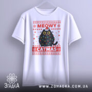 Футболка кіт на Різдво, біла, підвішена на вішалці, фон світло-сірий, принт з чорним котом у різдвяних гірляндах і шапці Санти, текст 'MEOWY CATMAS' червоним кольором.