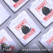 Футболка кіт на Різдво, біла, зображена на манекені, фон нейтральний, принт з чорним котом у різдвяних гірляндах і шапці Санти, текст 'MEOWY CATMAS' червоним кольором.