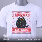 Футболка кіт на Різдво, біла, складена на поверхні, фон світлий, принт з чорним котом у різдвяних гірляндах і шапці Санти, текст 'MEOWY CATMAS' червоним кольором, з етикеткою на рукаві.