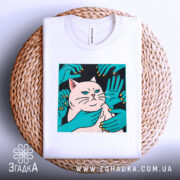 Футболка кіт незалежність, біла, складена на плетеній кошику, фон світло-сірий, принт з котом та руками, що його обіймають, яскраві кольори принта.