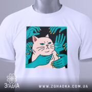 Футболка кіт незалежність, біла, складена на столі, фон світло-сірий, принт з котом та руками, що його обіймають, на етикетці зелена стрічка.