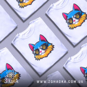 Футболка кіт патріот білого кольору, зображена на манекені, ракурс спереду, фон світло-сірий, принт з котом у сонцезахисних окулярах з жовто-блакитним гербом України.