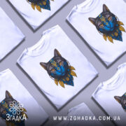 Футболка Кіт Патріот білого кольору, зображена на манекені, фон світло-сірий, принт з котом з блакитним обличчям та жовтими деталями, на грудях розташований герб України.