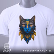 Футболка Кіт Патріот білого кольору, зображена на столі, ракурс зверху, фон світло-сірий, принт з котом з блакитним обличчям та жовтими деталями, на комірці видна етикетка.