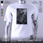 Футболка кіт проти динозавр, біла, зображена на манекені, фон світло-сірий, принт зображує кота, що лежить на спині, з динозаврами на задньому плані.