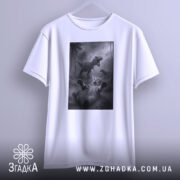 Футболка кіт проти динозавр, біла, підвішена на вішалці, фон світло-сірий, принт з котом, що лежить на спині, з динозаврами на задньому плані.