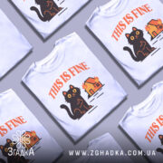 Футболка кіт this fine, біла футболка з принтом чорного кота, що сидить на фоні палаючого будинку, ракурс спереду, фон світлий, текст 'THIS IS FINE' виконаний оранжевим кольором.