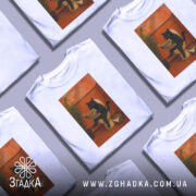 Футболка кіт вайб, біла футболка з принтом чорного кота, що сидить на унітазі, ракурс спереду, фон з градієнтом від світло-сірого до білого, деталі принта включають рослину та газету з написом 'НОВИНИ'.