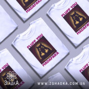 Футболка кіт з характером, біла, зображена на манекені, фон градієнтний сірий, принт з чорним котом, який показує два середніх пальці, текст 'FLUFF YOU MADAFAKA' у фіолетовому кольорі.