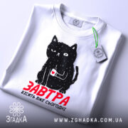 Футболка кіт з написом, біла, зображена з верхнього ракурсу, фон світлий, принт з чорним котом, який тримає чашку з серцем, текст червоним шрифтом 'ЗАВТРА БІСІТЬ ВЖЕ СЬОГОДНІ', на комірці видно етикетку.
