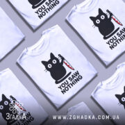 Футболка кіт з ножем, біла, зображена на манекені, фон градієнтний сірий, принт з чорним котом, що тримає ніж, текст "YOU SAW NOTHING" чорним шрифтом під котом.