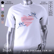 Футболка кохай птахи, біла, зображена з правого боку, на фоні світло-сірого кольору, принт з двома журавлями, що летять, на рожевому серці з написом 'Кохай'.