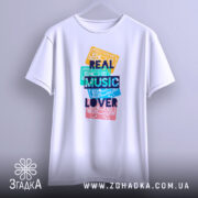 Футболка кольорові касети, біла, зображена з бокового ракурсу на вішалці, фон світлий, принт з кольоровими касетами та написом 'REAL MUSIC LOVER' у темно-синьому кольорі.