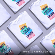 Футболка кольорові касети, біла, зображена з фронтального ракурсу на манекені, фон нейтральний, принт складається з кольорових касет з написом 'REAL MUSIC LOVER' у темно-синьому кольорі.