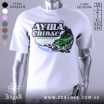 Футболка коли клює, біла, зображена на манекені, фон світло-сірий, принт з рибою та текстом "ДУША СПІВАЄ КОЛИ КЛЮЄ" в зелених та чорних кольорах.