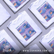 Футболка коли темно, біла, зображена з фронтального ракурсу, фон нейтральний, принт містить чотири комікси з персонажами, один з яких синій, а інший - хлопчик з рудим волоссям.