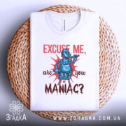Футболка комічний маніяк, біла, складена на плетеній кошику, фон світло-сірий, принт з персонажем у масці, що тримає трубку, текст червоним кольором.