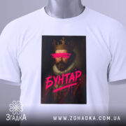 Футболка король бунтар, біла, зображена зверху, на фоні світло-сірого градієнта, принт з портретом короля, з рожевими мазками на очах та написом 'БУНТАР', з етикеткою зеленого кольору.