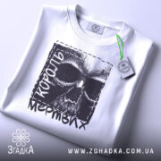 Футболка король мертвих, біла, складена на поверхні, з видимим етикеткою, фон світло-сірий, принт з черепом та текстом 'король мертвих' у чорному кольорі.