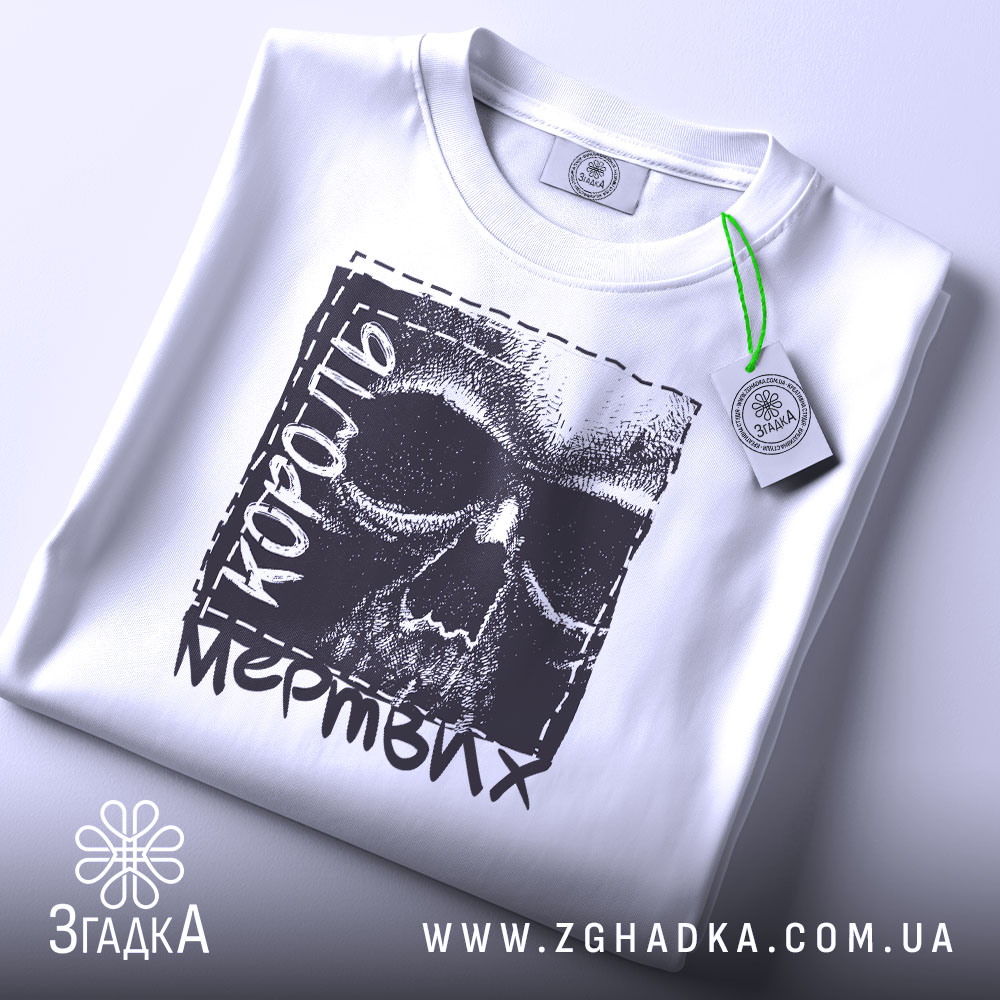 Футболка король мертвих, біла, складена на поверхні, з видимим етикеткою, фон світло-сірий, принт з черепом та текстом 'король мертвих' у чорному кольорі.