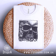 Футболка король мертвих, біла, складена на плетеній кошику, фон світло-сірий, принт з черепом та текстом 'король мертвих' у чорному кольорі.