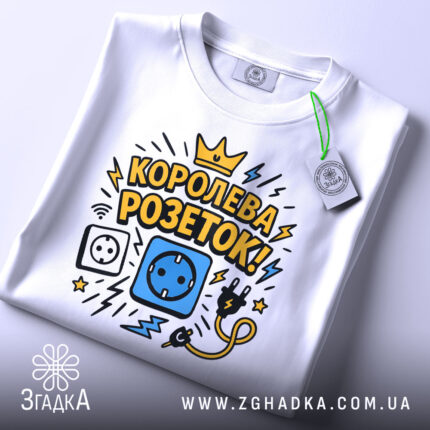Футболка королева розеток білого кольору, зображена зверху, на фоні світло-сірого кольору, принт з малюнками розетки, електричного шнура та блискавок, текст "КОРОЛЕВА РОЗЕТОК!" у жовтому та чорному кольорах, на футболці є етикетка.