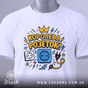 Футболка королева розеток білого кольору, зображена зверху, на фоні світло-сірого кольору, принт з малюнками розетки, електричного шнура та блискавок, текст "КОРОЛЕВА РОЗЕТОК!" у жовтому та чорному кольорах, на футболці є етикетка.