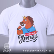 Футболка королівський жеребець, білого кольору, лежить на плоскій поверхні, фон світло-сірий, принт з конем у короні, що демонструє м'язи, з написом 'Королівський жеребець', на футболці є етикетка з зеленим шнурком.