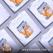 Футболка котани з новим роком, біла, зображена на манекені, фон світло-сірий, принт з веселим котом у червоній шапці та сердечками.