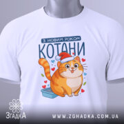 Футболка котани з новим роком, біла, зображена зверху, фон світло-сірий, принт з котом у червоній шапці, на футболці є етикетка з зеленим шнурком.