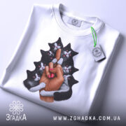 Футболка котяча любов, біла, складена на столі, фон світлий, принт зображає руку з манікюром, що тримає кілька чорних котів, коти з виразами радості, на футболці є етикетка.