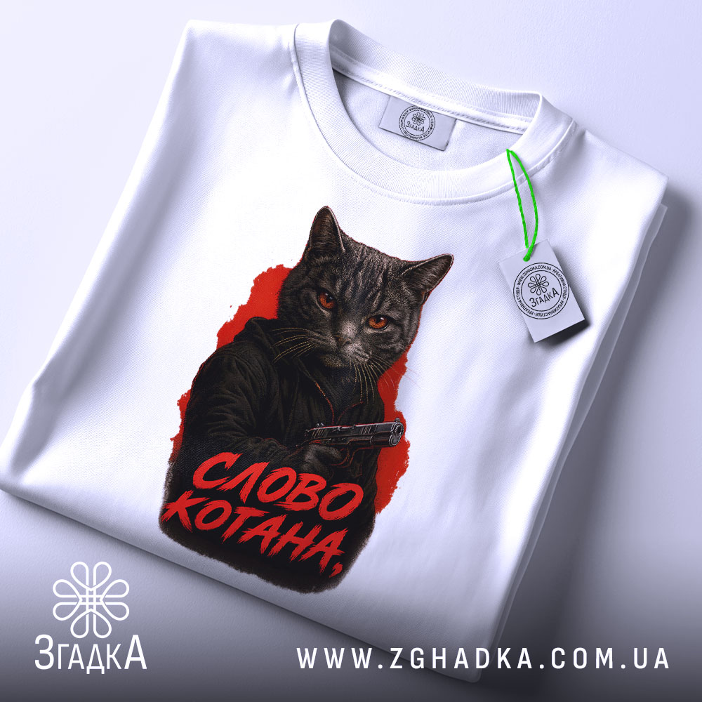 Футболка котяча мафія, біла футболка на столі, фон світло-сірий, принт з котом у чорному капюшоні з пістолетом, текст 'СЛОВО КОТАНА' червоним кольором, на футболці є етикетка.