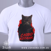 Футболка котяча мафія, біла футболка на столі, фон світло-сірий, принт з котом у чорному капюшоні з пістолетом, текст 'СЛОВО КОТАНА' червоним кольором, на футболці є етикетка.