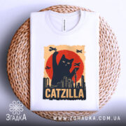 Футболка котяча монстр білого кольору, зображена зверху на плетеній кошику, фон світло-сірий, принт з чорним котом, що піднімає лапу на фоні червоного сонця та силуетів міста.