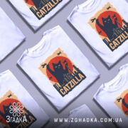 Футболка котяча монстр білого кольору, зображена з фронтального ракурсу на манекені, фон світло-сірий, принт з чорним котом, що піднімає лапу на фоні червоного сонця та силуетів міста.