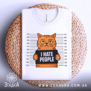 Футболка котячий гумор хейт, складена біла футболка на плетеній основі, з принтом кота, що тримає табличку з написом 'I HATE PEOPLE', фон білий, принт яскравий, видно етикетку з логотипом.