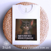 Футболка котячий настрій, біла, зображена зверху на плетеній кошику, фон білий, принт з котом з усмішкою та текстом "ЩО Б ВИ БЕЗ МЕНЕ РОБИЛИ".